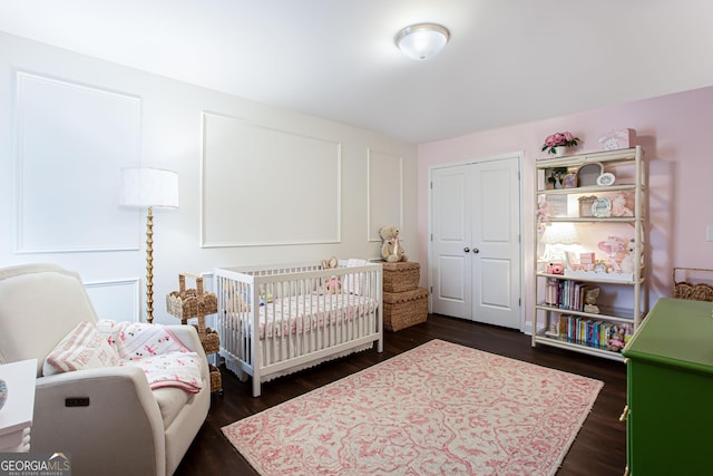 bedroom with dark wood-type flooring, a nursery area, and a closet