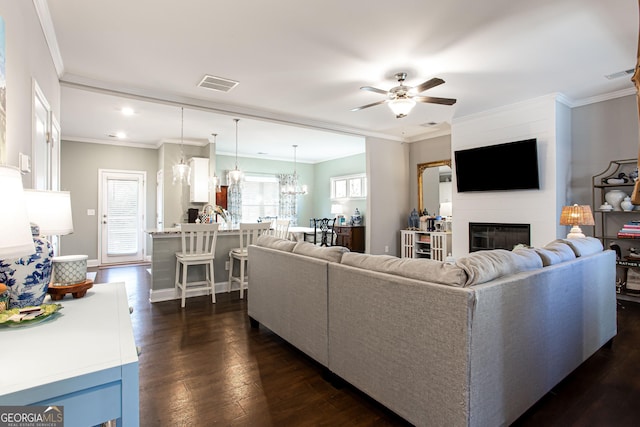 living room featuring dark wood finished floors, visible vents, crown molding, and a glass covered fireplace