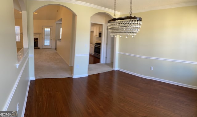 unfurnished dining area with ornamental molding, wood finished floors, arched walkways, and a fireplace with raised hearth