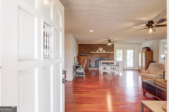 living room with brick wall, ceiling fan, a fireplace, wood finished floors, and a textured ceiling