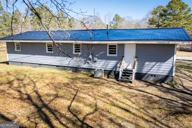 rear view of property with crawl space, entry steps, metal roof, and a yard