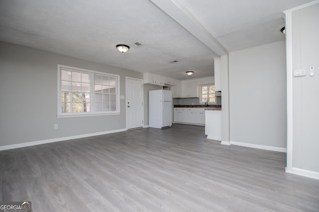 unfurnished living room featuring a sink, visible vents, baseboards, and dark wood finished floors