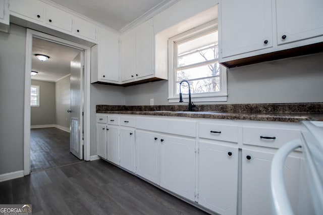 kitchen with a wealth of natural light, ornamental molding, dark countertops, dark wood finished floors, and white cabinetry