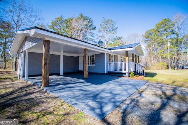 view of side of property with an attached carport, driveway, a porch, a lawn, and metal roof