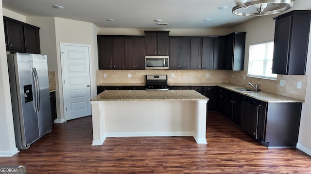 kitchen with light stone counters, a kitchen island, dark wood finished floors, a sink, and stainless steel appliances