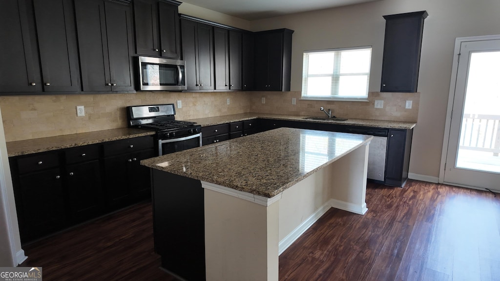 kitchen with a sink, light stone counters, appliances with stainless steel finishes, and dark wood-style flooring