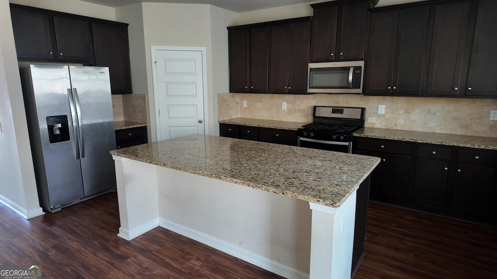 kitchen featuring appliances with stainless steel finishes, a center island, dark wood-type flooring, and light stone countertops