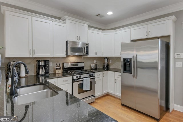 kitchen with light wood finished floors, a sink, white cabinets, appliances with stainless steel finishes, and crown molding