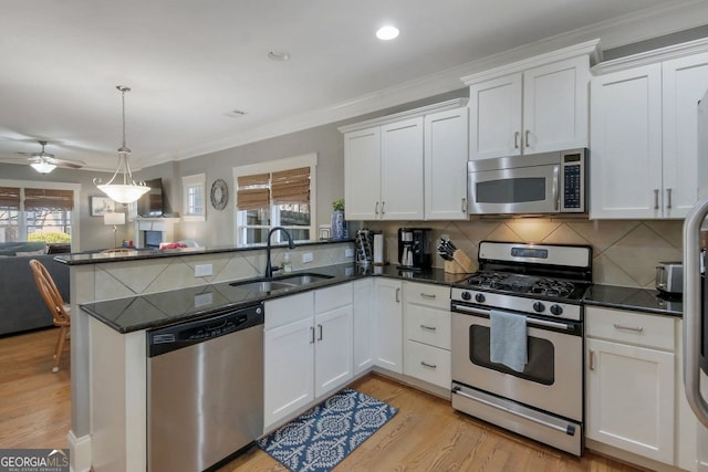 kitchen with open floor plan, a peninsula, stainless steel appliances, white cabinetry, and a sink