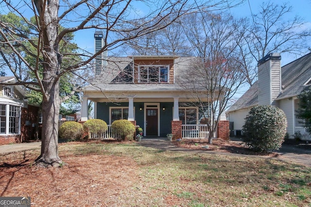 view of front facade featuring a chimney, covered porch, and a front lawn