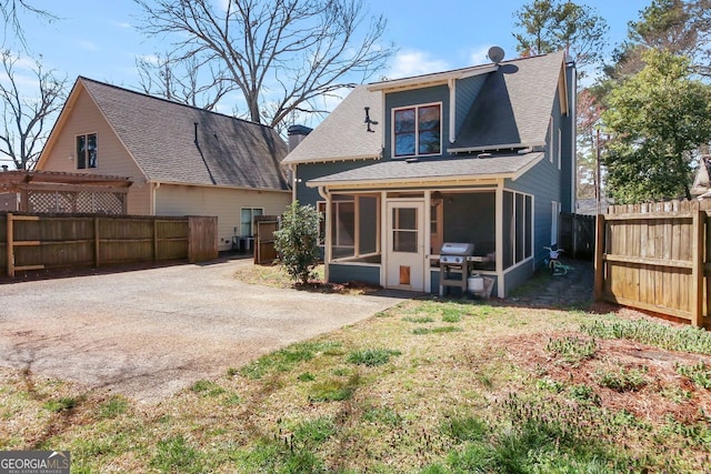 rear view of house featuring a yard, fence, a shingled roof, and a sunroom