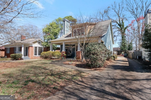 view of front of home featuring a porch, a chimney, a front lawn, central air condition unit, and brick siding