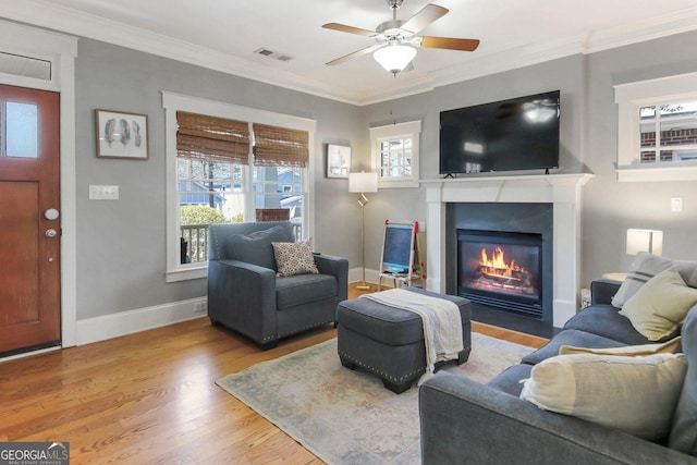 living room with visible vents, baseboards, a fireplace with flush hearth, ornamental molding, and wood finished floors