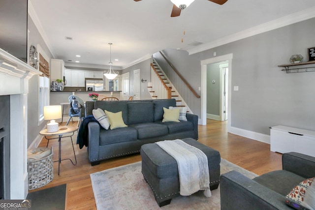 living area featuring stairway, a fireplace with raised hearth, crown molding, and light wood finished floors