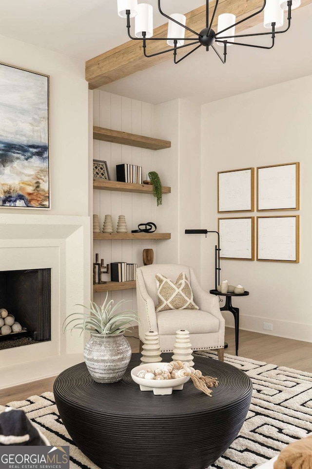 interior space with wood finished floors, baseboards, beam ceiling, a fireplace with raised hearth, and a chandelier