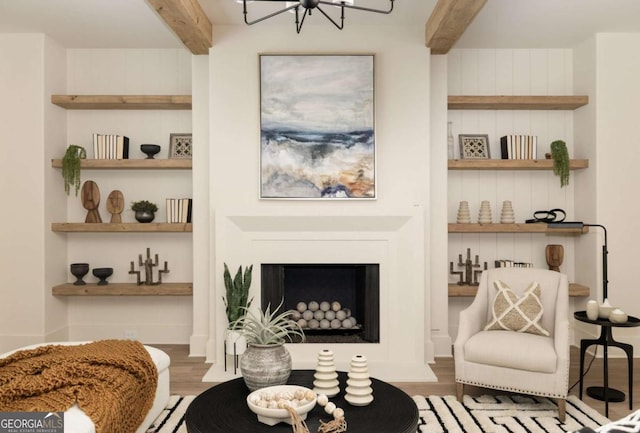 sitting room featuring beamed ceiling, a fireplace, an inviting chandelier, and wood finished floors