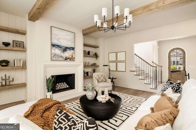 living area with wood finished floors, a fireplace with raised hearth, arched walkways, beamed ceiling, and a chandelier