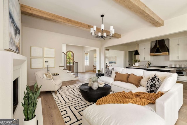 living area featuring baseboards, a fireplace, light wood-style floors, beamed ceiling, and a chandelier