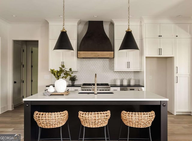 kitchen featuring backsplash, a center island with sink, light wood finished floors, and custom range hood