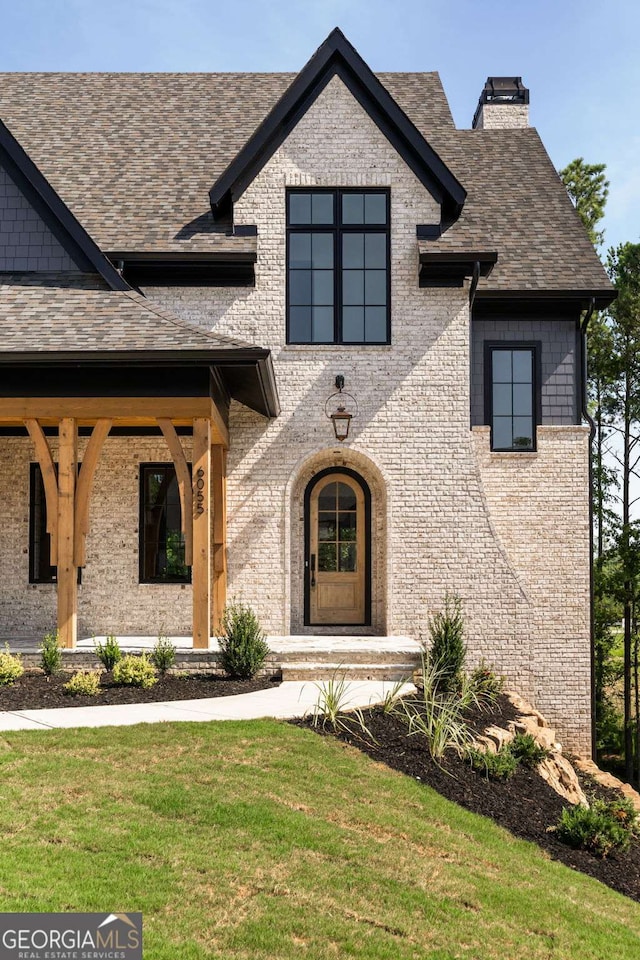 view of front of house featuring a front yard, a chimney, brick siding, and a shingled roof