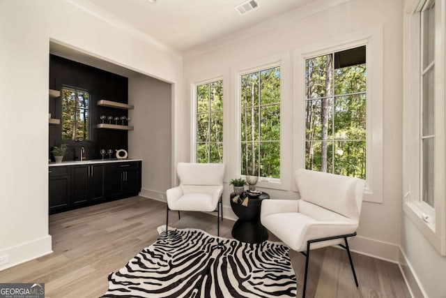 living area featuring baseboards, light wood-type flooring, wet bar, and visible vents