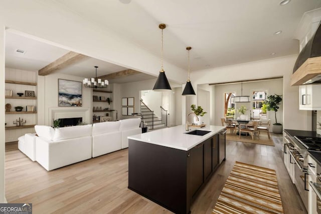 kitchen with beamed ceiling, a center island with sink, a fireplace, light wood-style floors, and a sink