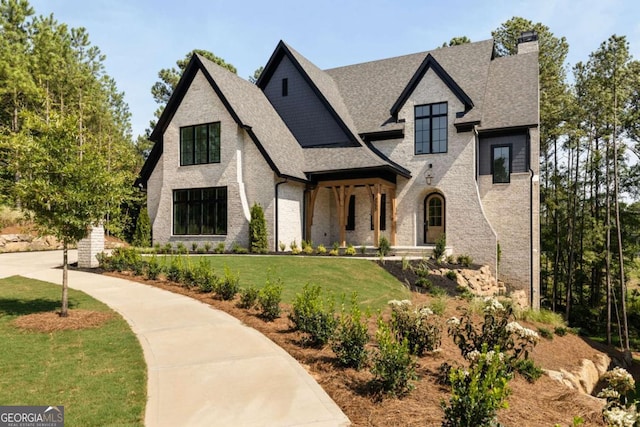 view of front of property with brick siding, a chimney, a front lawn, and roof with shingles