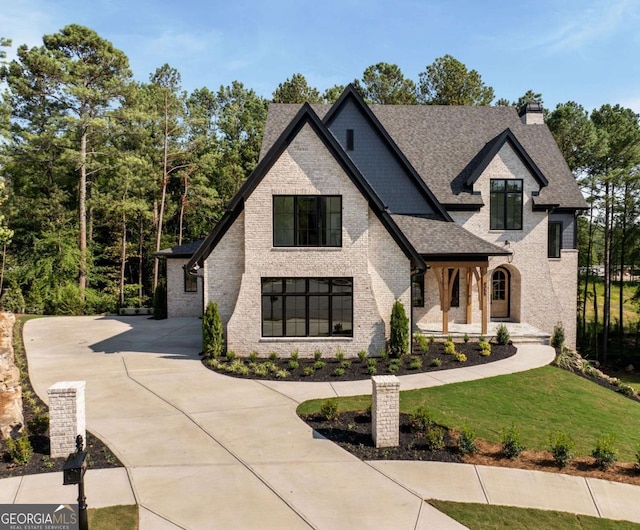 french country home with driveway, a shingled roof, a chimney, a front lawn, and brick siding