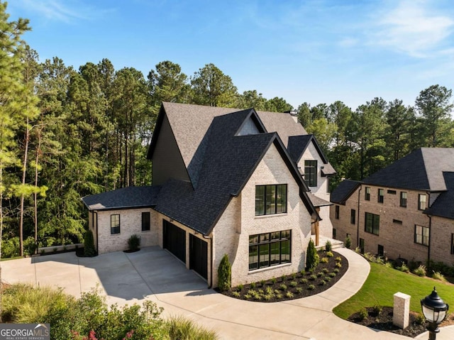 french country home with brick siding, a shingled roof, a front lawn, concrete driveway, and an attached garage