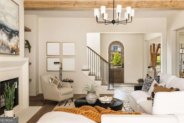 living room featuring a notable chandelier, a fireplace with raised hearth, stairway, and wood finished floors