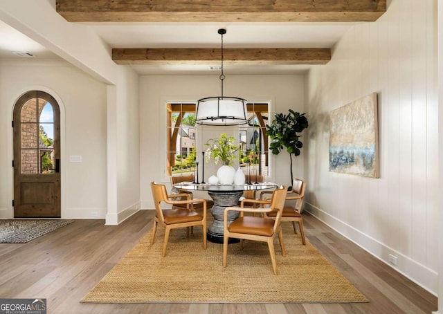 dining space with beam ceiling, arched walkways, baseboards, and wood finished floors