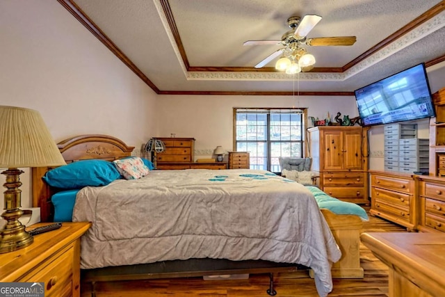 bedroom with wood finished floors, a tray ceiling, ceiling fan, ornamental molding, and a textured ceiling