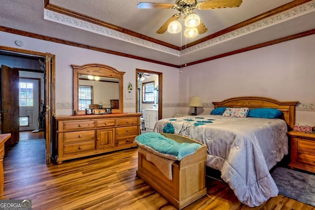 bedroom featuring light wood finished floors, crown molding, a textured ceiling, and a raised ceiling