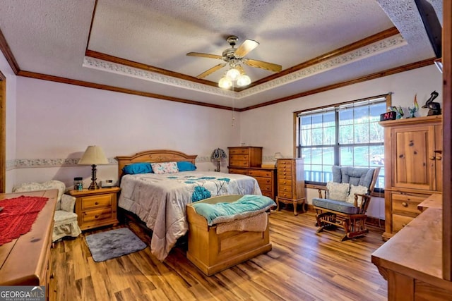 bedroom with light wood finished floors, a textured ceiling, crown molding, and a tray ceiling