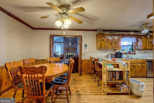 dining space featuring light wood-style floors, a textured ceiling, wainscoting, and wallpapered walls