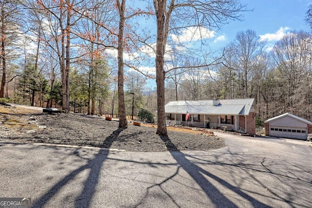 view of front of property with an outbuilding, covered porch, metal roof, a garage, and brick siding