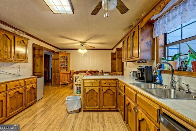 kitchen featuring a peninsula, light wood-style flooring, ornamental molding, a sink, and stainless steel dishwasher