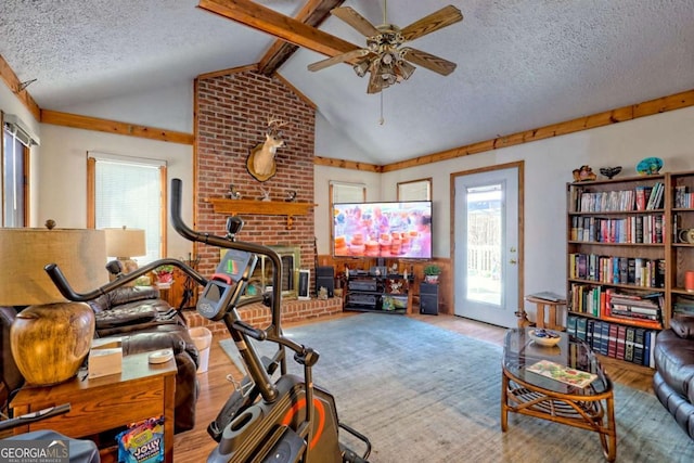 workout area featuring a ceiling fan, a textured ceiling, wood finished floors, lofted ceiling, and a brick fireplace