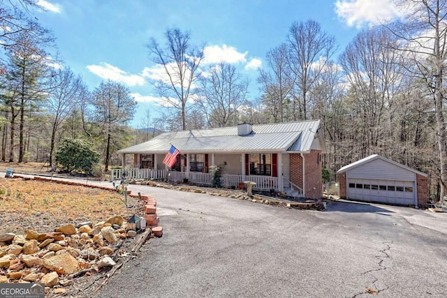 view of front facade featuring an outbuilding, a porch, a chimney, a garage, and metal roof