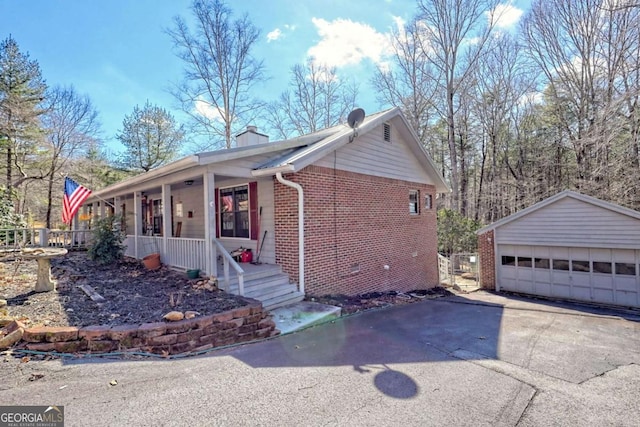 view of front of home featuring an outbuilding, covered porch, a chimney, a detached garage, and brick siding