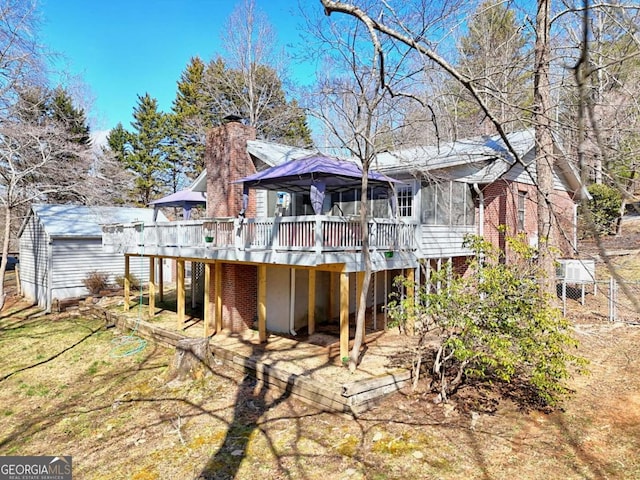 rear view of property with a wooden deck, a sunroom, a chimney, an outdoor structure, and brick siding