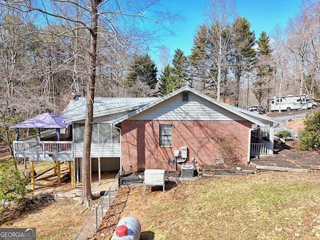 back of property featuring a wooden deck, brick siding, central AC unit, and a sunroom