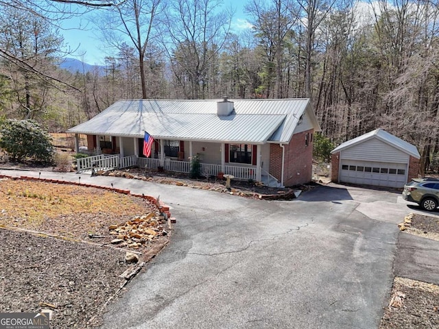 ranch-style home with an outbuilding, covered porch, a detached garage, brick siding, and metal roof