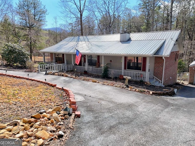 view of front of home featuring brick siding, a porch, metal roof, a chimney, and driveway