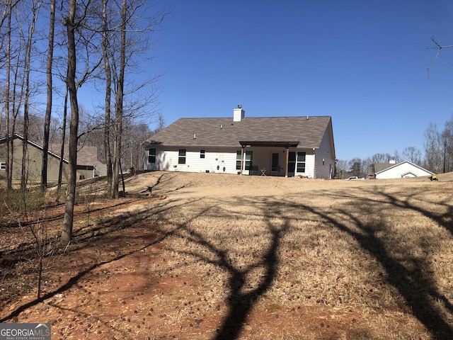 back of house with a chimney and a shingled roof