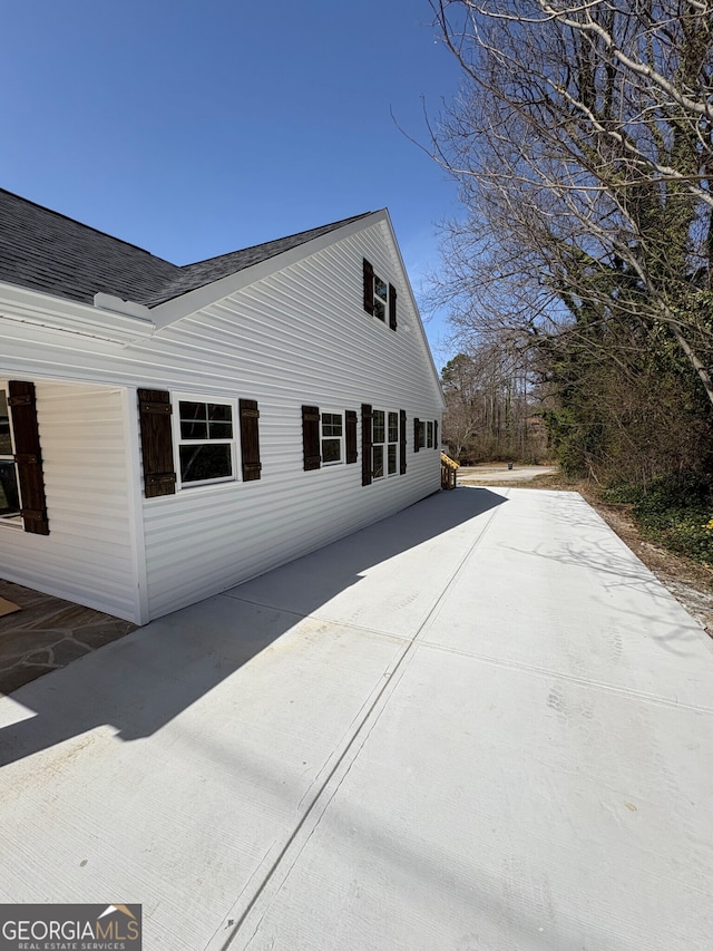 view of side of property featuring a patio area and a shingled roof