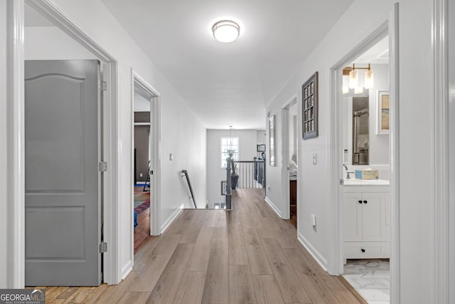 hallway featuring an upstairs landing, baseboards, and light wood finished floors