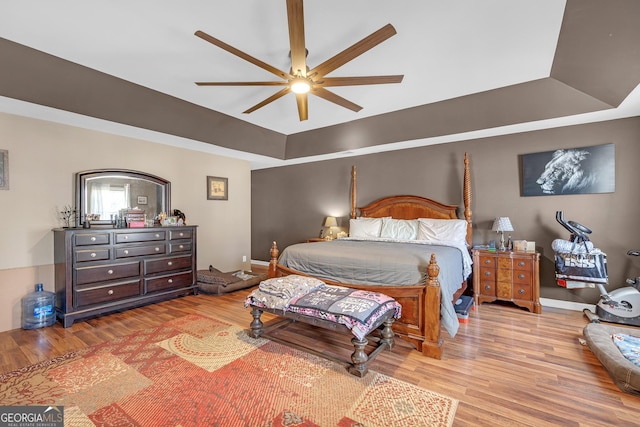 bedroom with baseboards, a raised ceiling, ceiling fan, and wood finished floors