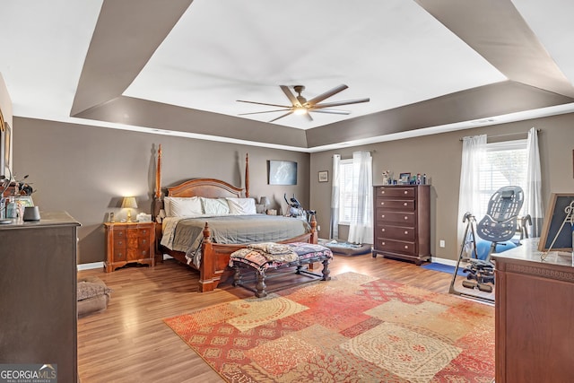 bedroom with a tray ceiling, a ceiling fan, baseboards, and light wood finished floors