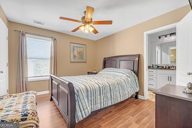 bedroom featuring visible vents, a ceiling fan, ensuite bath, light wood finished floors, and baseboards